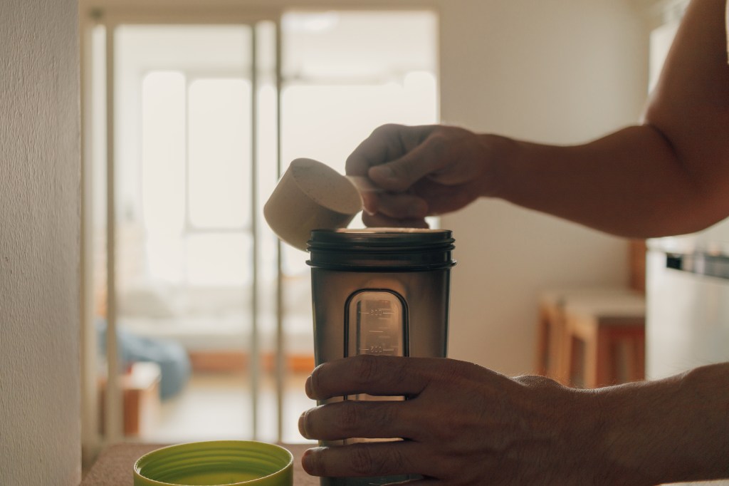 A man putting whey protein powder into a shaker.