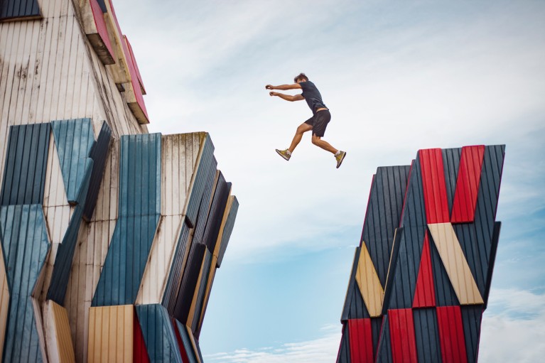 A man leaping between two tall platforms in a modern industrial building