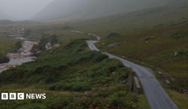 A large green landscape with a river on the left of the image and a road running  on the right hand side. The road disappears into the distance and it's a misty day.