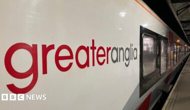 Side view of a Greater Anglia train with carriages running the length of the platform at a station