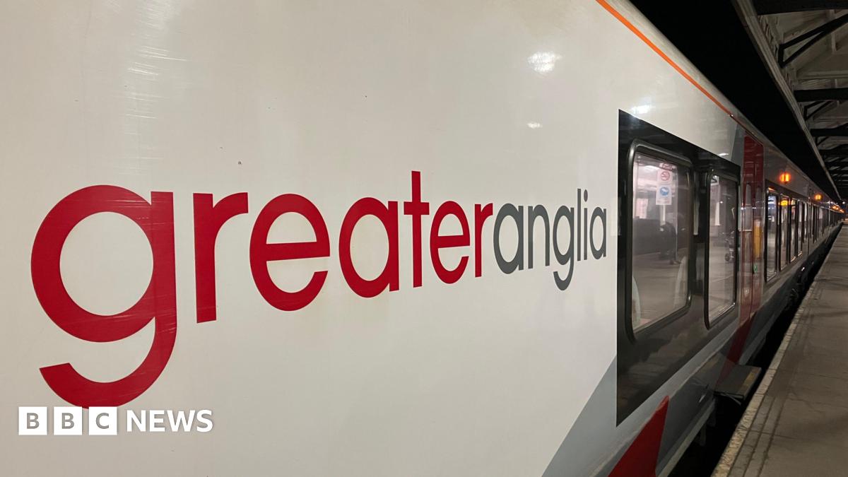 Side view of a Greater Anglia train with carriages running the length of the platform at a station