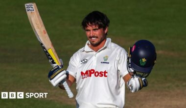 A smiling Kiran Carlson acknowledges the crowd with bat in one hand and helmet in the other