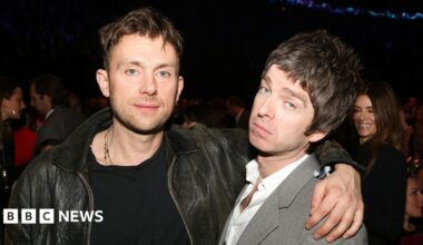 Damon Albarn wearing a black leather jacket with his arm around Noel Gallagher at the Brit Awards 2013