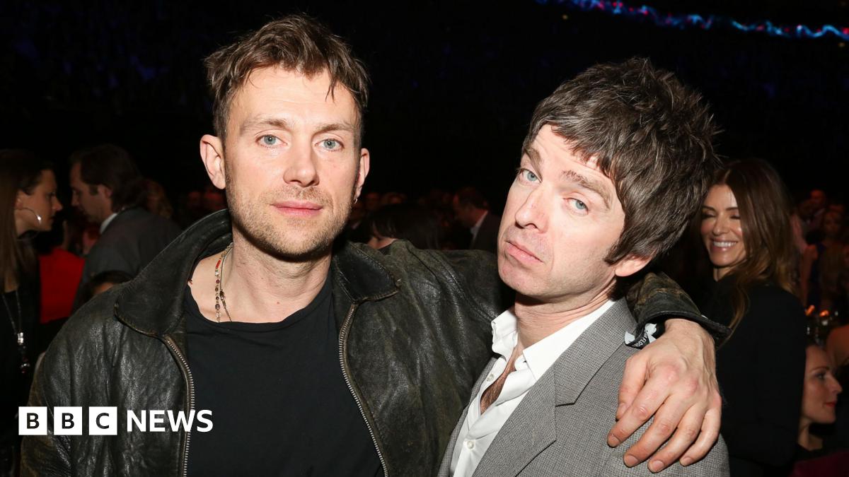 Damon Albarn wearing a black leather jacket with his arm around Noel Gallagher at the Brit Awards 2013