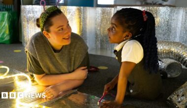 Two girls in blue uniforms are focused on etching designs into metal plates