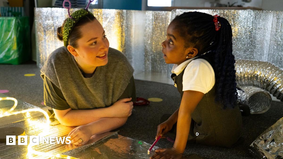 Two girls in blue uniforms are focused on etching designs into metal plates