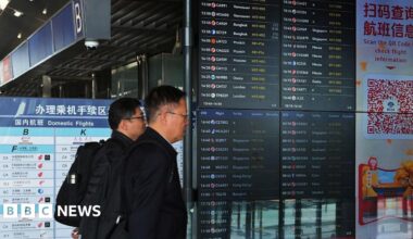 Two men walk past departures board at Beijing airport