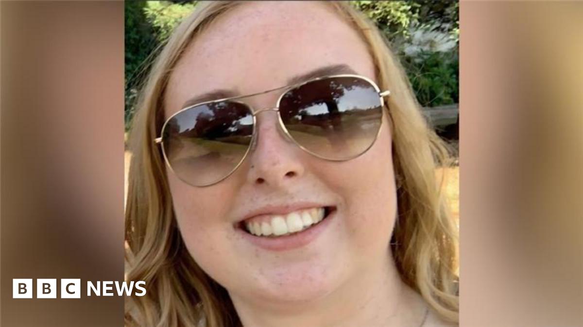 A photograph of Stephanie Irons, a 23-year-old white woman. Se is smiling, wearing aviator style sunglasses and has wavy hair