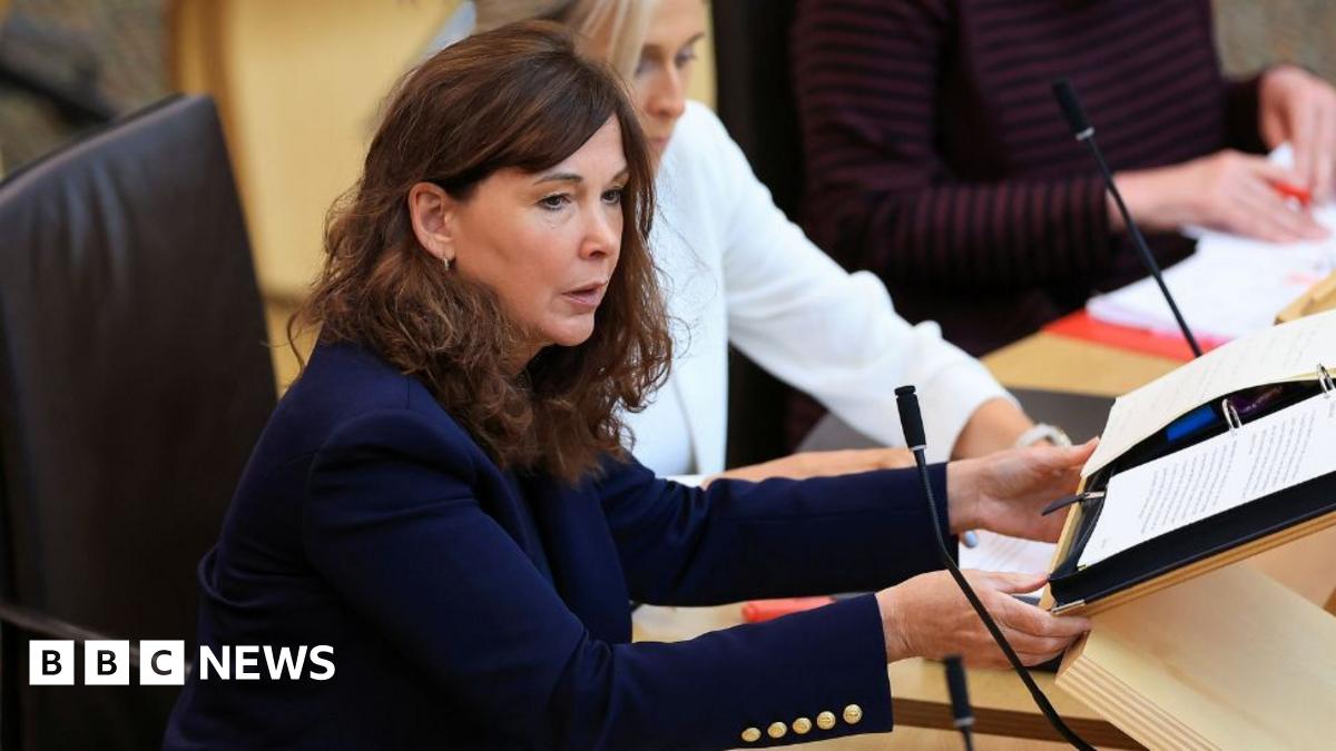 Peter Murrell looking off to his right while sitting in a room. He is wearing a black suit, white shirt and dark coloured tie.