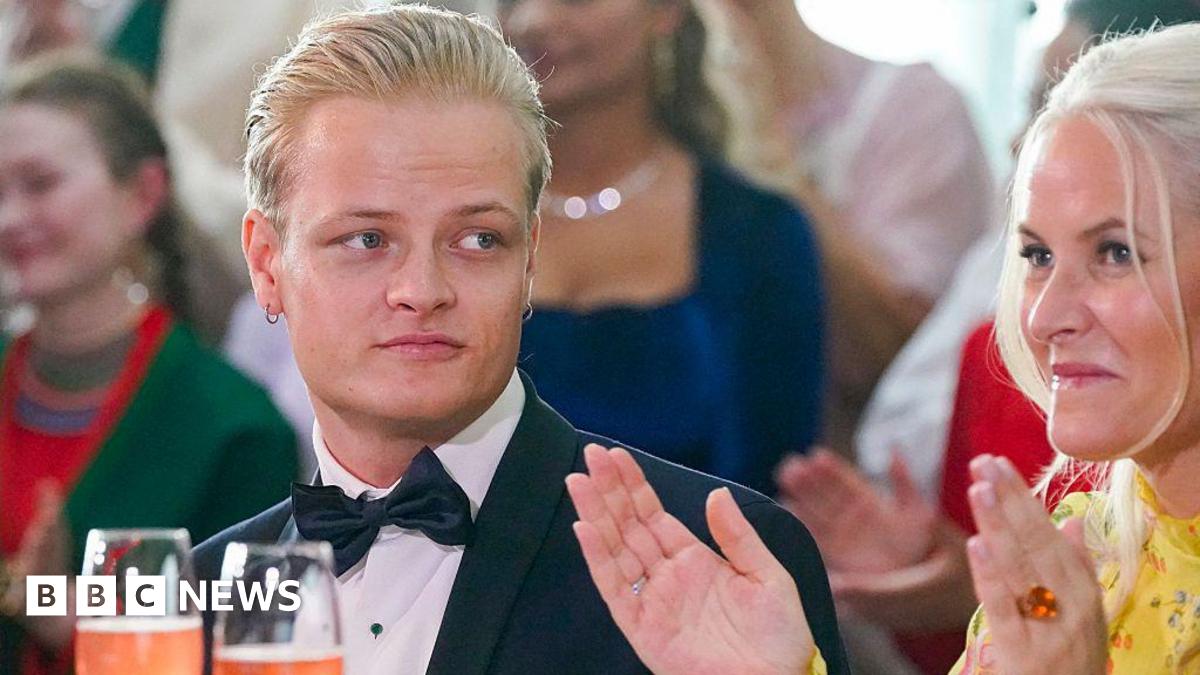 A young man with blond hair and a bow tie looks on as a woman in a yellow dress claps