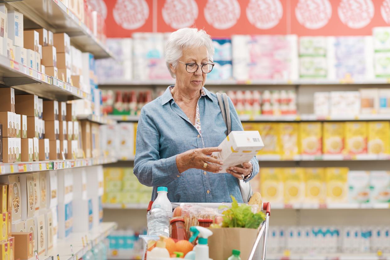 Senior woman doing grocery shopping, she is reading information on a product package