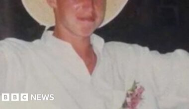 Young man wearing a white outfit and a wide brimmed white hat smiling to camera