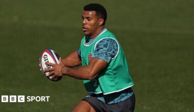 Immanuel Feyi-Waboso running with the ball during an England training camp. He has short black hair and is wearing a green bib with a blue training top and shorts.