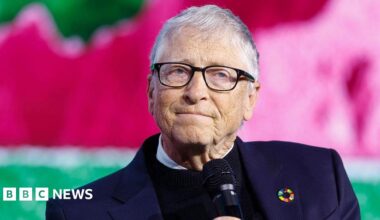 Microsoft co-founder Bill Gates, wearing a blue suit and holding a microphone as he looks away from the camera.