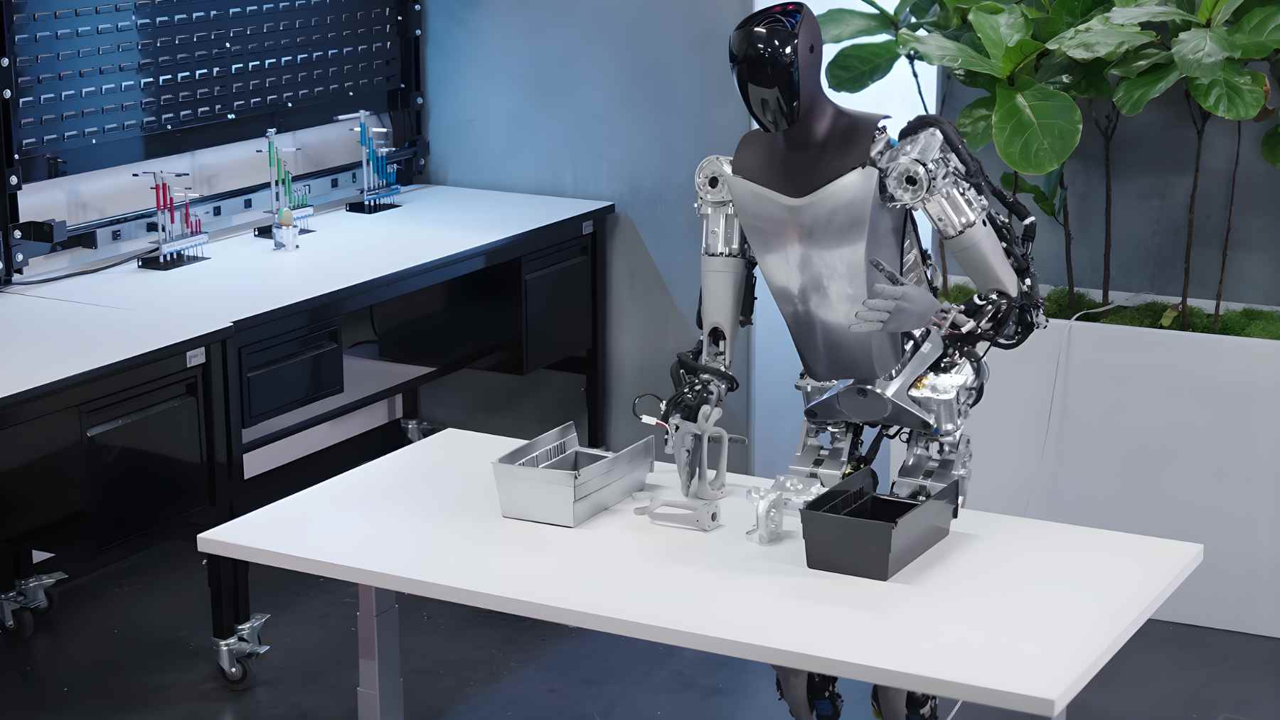 Tesla’s Optimus humanoid robot works at a lab table during a demo, showing AI-driven hands handling small parts.