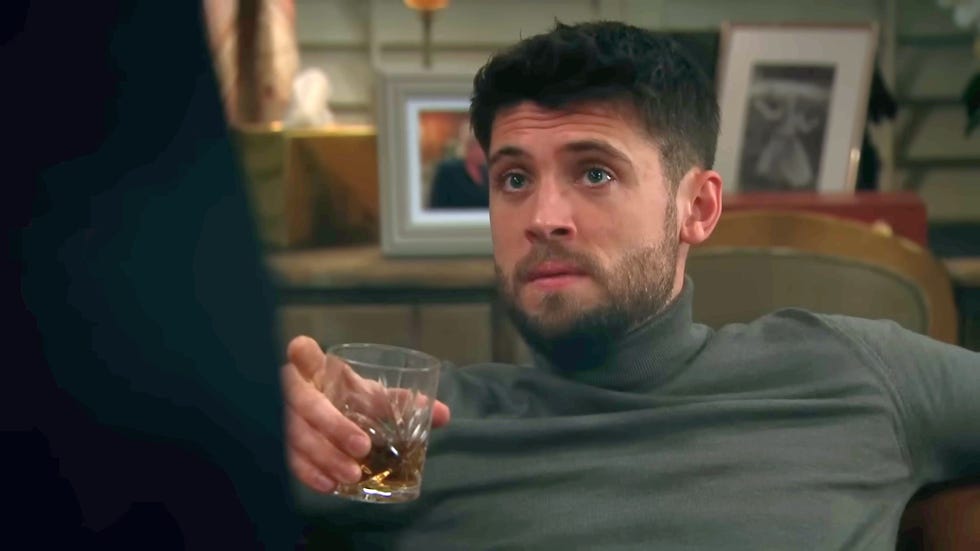 emmerdale, joe tate sitting back in a chair drinking from a glass tumbler