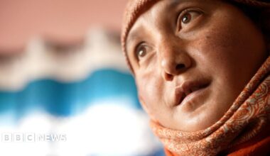 Five women wearing winter jackets look into the camera. They are standing in front of snow-covered peaks.