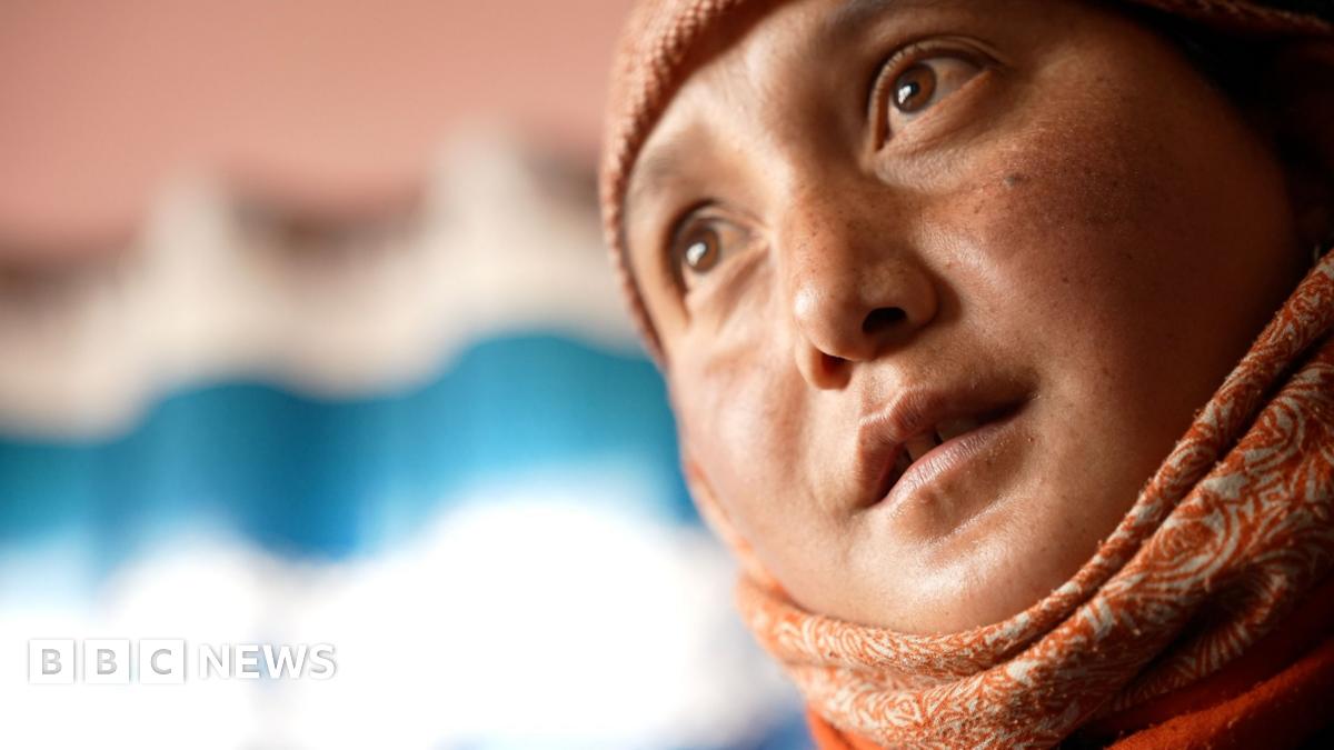 Five women wearing winter jackets look into the camera. They are standing in front of snow-covered peaks.