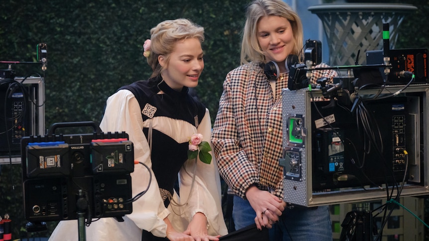 Two blond women, one in a puffy wedding dress sit on a blue couch