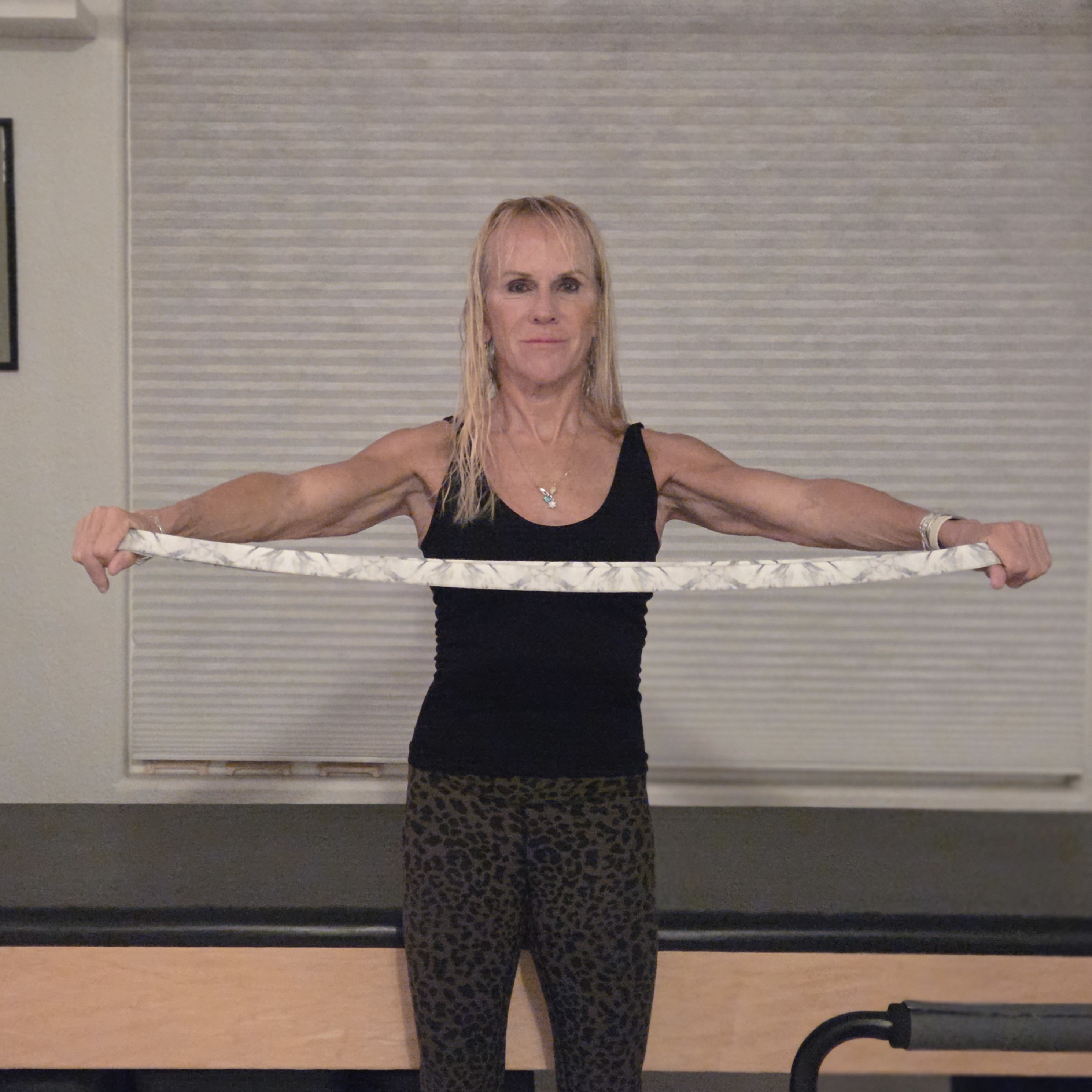 Woman stretching with yoga strap in front of a Pilates reformer bed