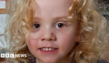 A young boy with blond curly hair and brown eyes, looking directly at camera and smiling