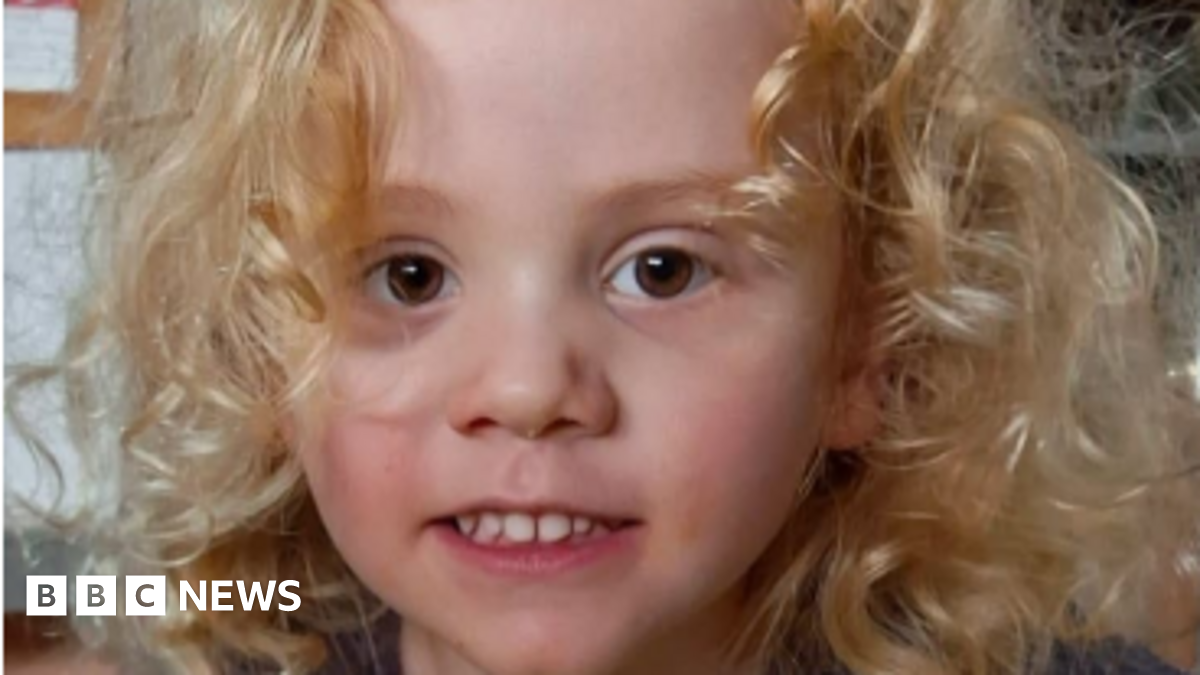 A young boy with blond curly hair and brown eyes, looking directly at camera and smiling