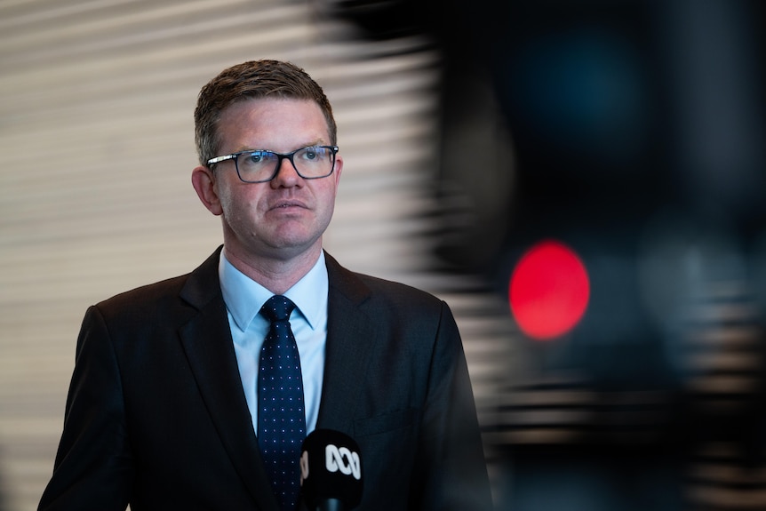 A man with glasses addresses the media.