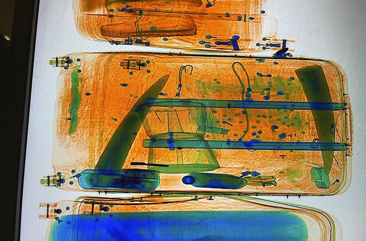 An image with artificial coloring shows the contents of a suitcase, including two long pointed solid objects.