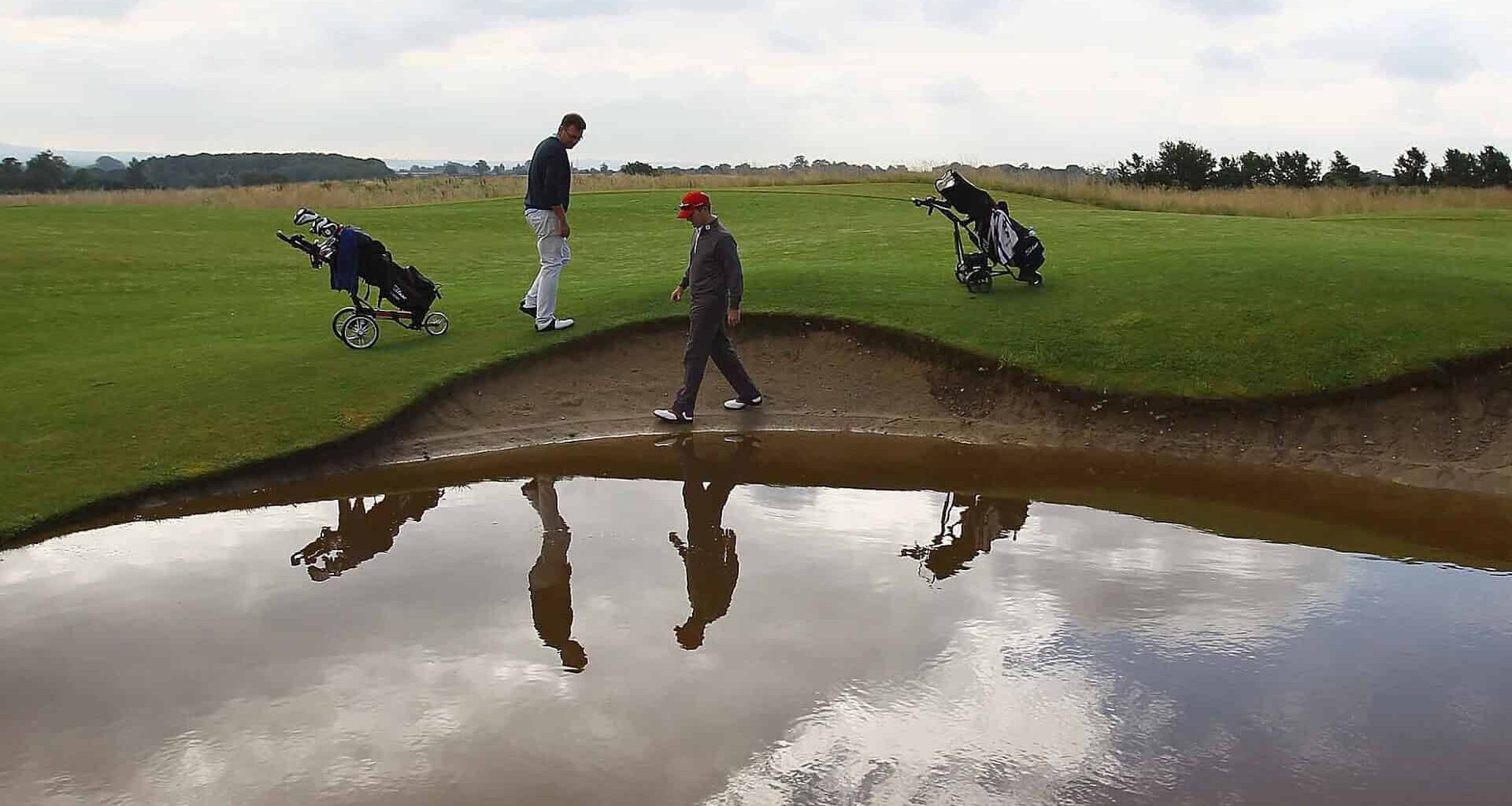 John Jacobs (L) of Cumberwell Park Golf Club looks for his ball in a flooded bunker with Richard Dinsdale of Parc Golf Academy during the Lombard Challenge Regional Qualifier at Cumberwell Park Golf Club on August 6, 2012 in Bath, England