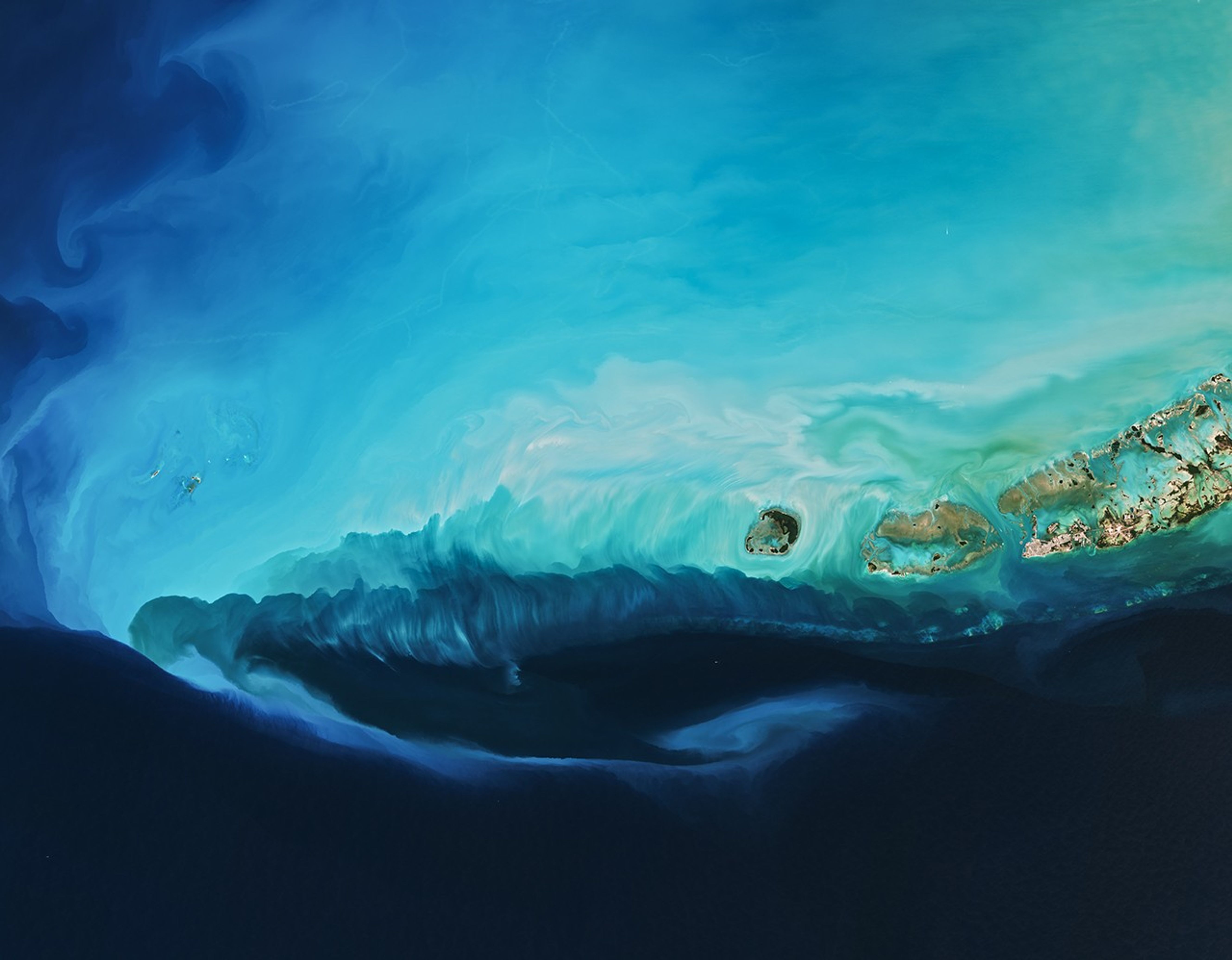 The water north of the Florida Keys appears bright blue to white. To the south, it is dark blue except for a long, narrow bright band running from west to east.