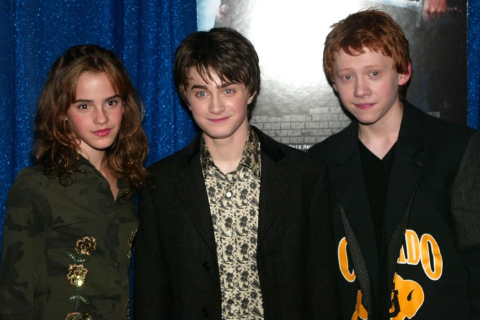 harry-potter-tv-series Emma Watson, Daniel Radcliffe and Rupert Grint stood smiling for a photo. They are all stood next to each other in front of a poster