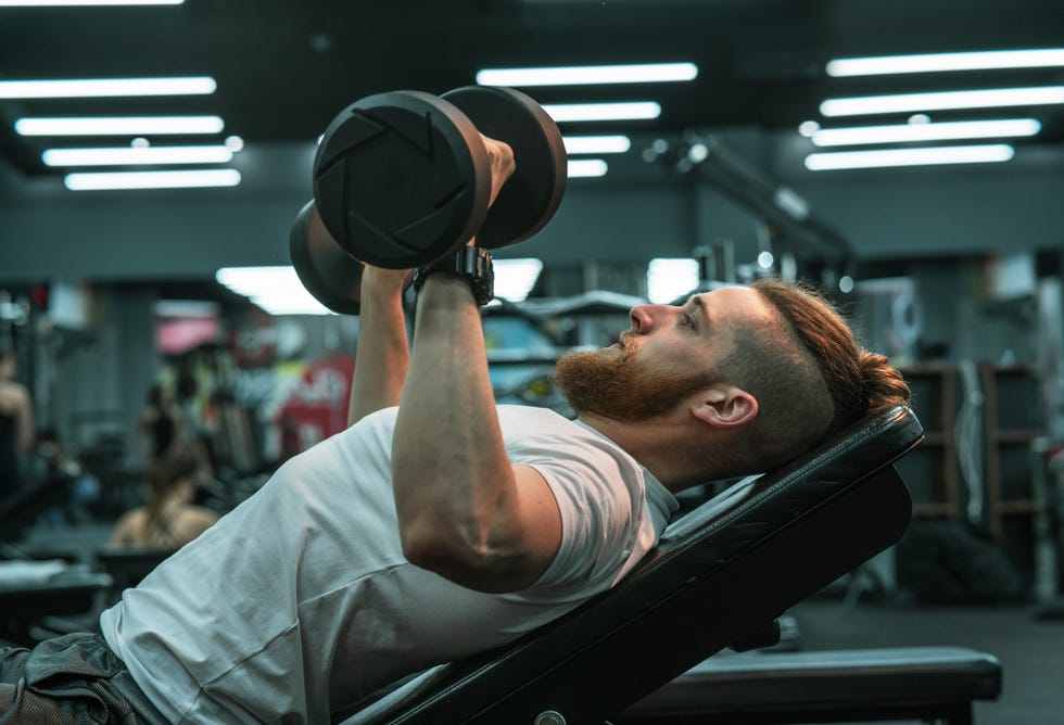 A man in sportswear lies on the gym bench and workout on his chest and arms with dumbbells. a man in sportswear lies on the gym bench and workout on his chest and arms with dumbbells.