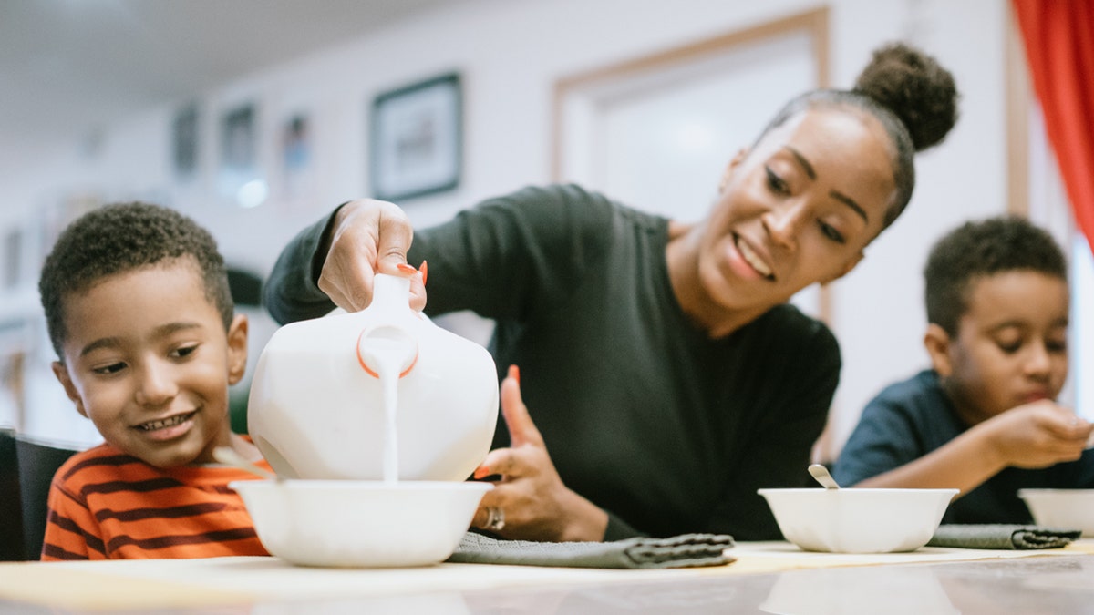 mom pours milk into her son's cereal bowl
