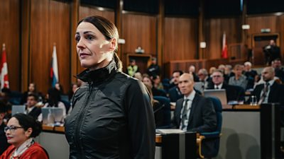 First look from Vigil series three. DCI Amy Silva (Suranne Jones) stands in a courtroom. Officials in formal clothing are seated in the background. 