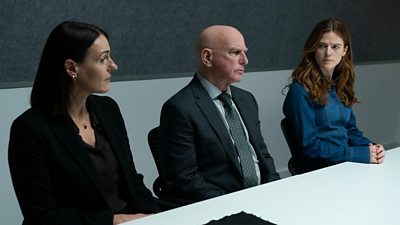 First look from Vigil series three. DCI Amy Silva (Suranne Jones), DS Robertson (Gary Lewis) and DI Kirsten Longacre (Rose Leslie) sit at a table wearing formal clothing. 
