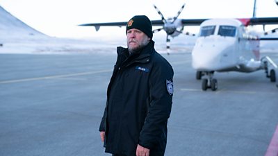 First look from Vigil series three. A man stands on a runway beside snow-covered hills. A propeller plane sits on the runway behind him. 
