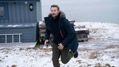 First look from Vigil series three. A man runs outdoors across snow-covered terrain. He wears warm clothing. A house is visible in the background. 