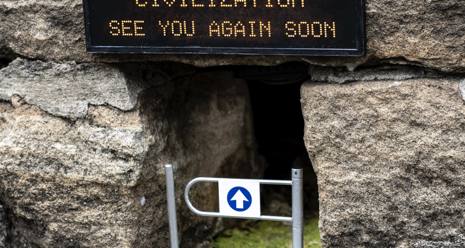 A miniature installation by Michael Pederson of a gap at the base of a stone wall with a gate and a replica digital sign that reads