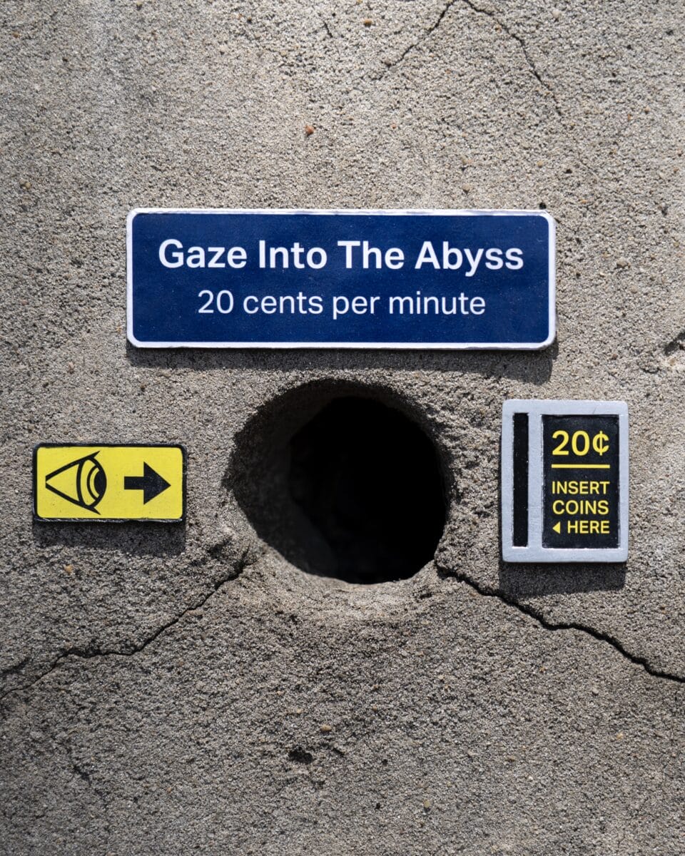An up-close view of a miniature installation by Michael Pederson of tiny signs installed next to a circular hole in a concrete wall, which read