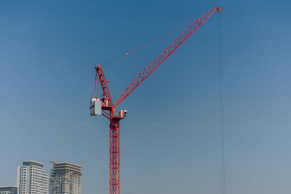 Red construction crane towering against a clear blue sky with modern buildings under construction visible in the background Red construction crane towering against a clear blue sky with modern buildings under construction visible in the background