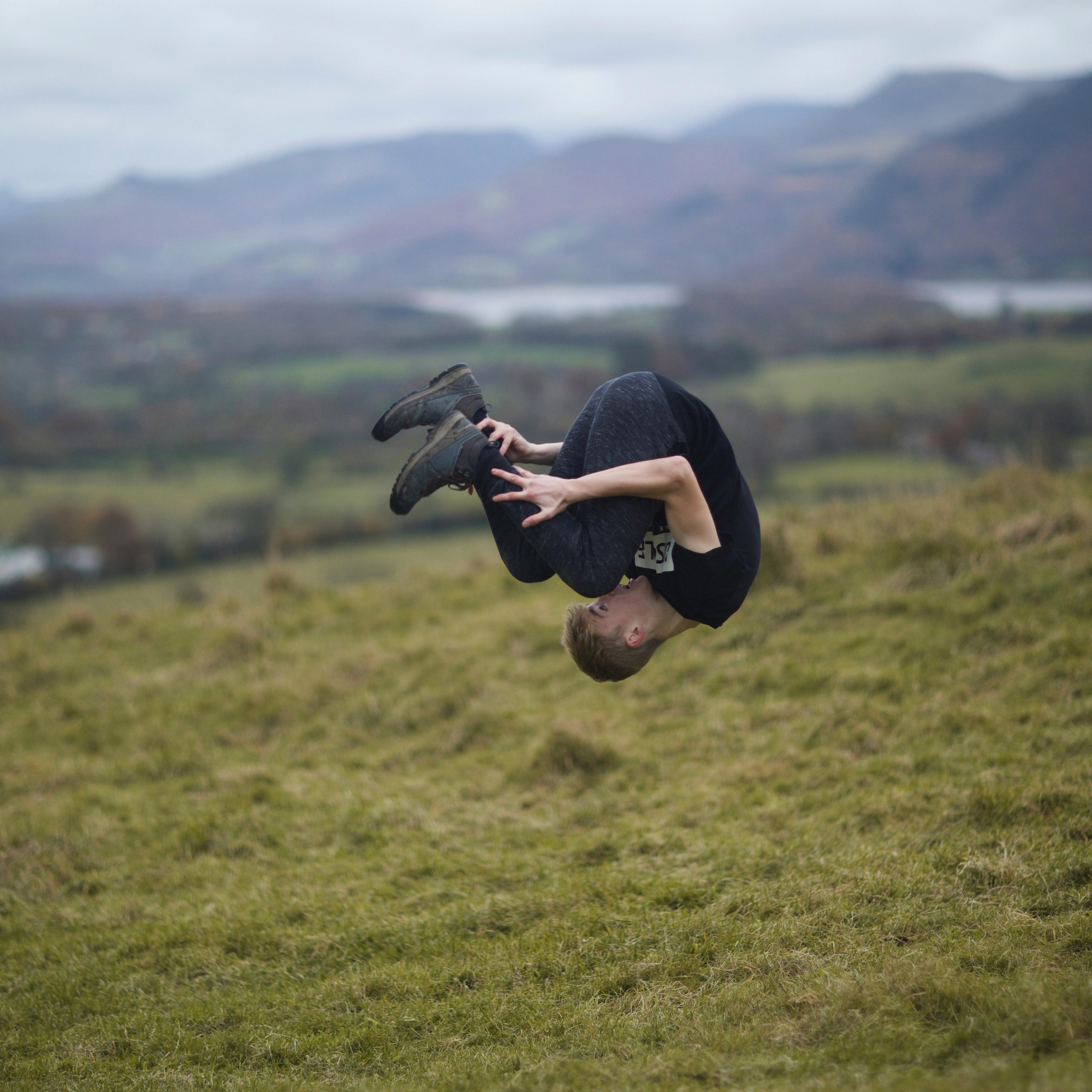 A person in the air, mid-flip, on a grassy hill with distant hills in the background.