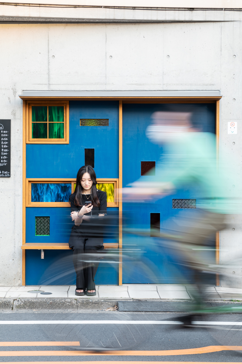 colored glass apertures reveal lively tokyo bar through bright blue entrance