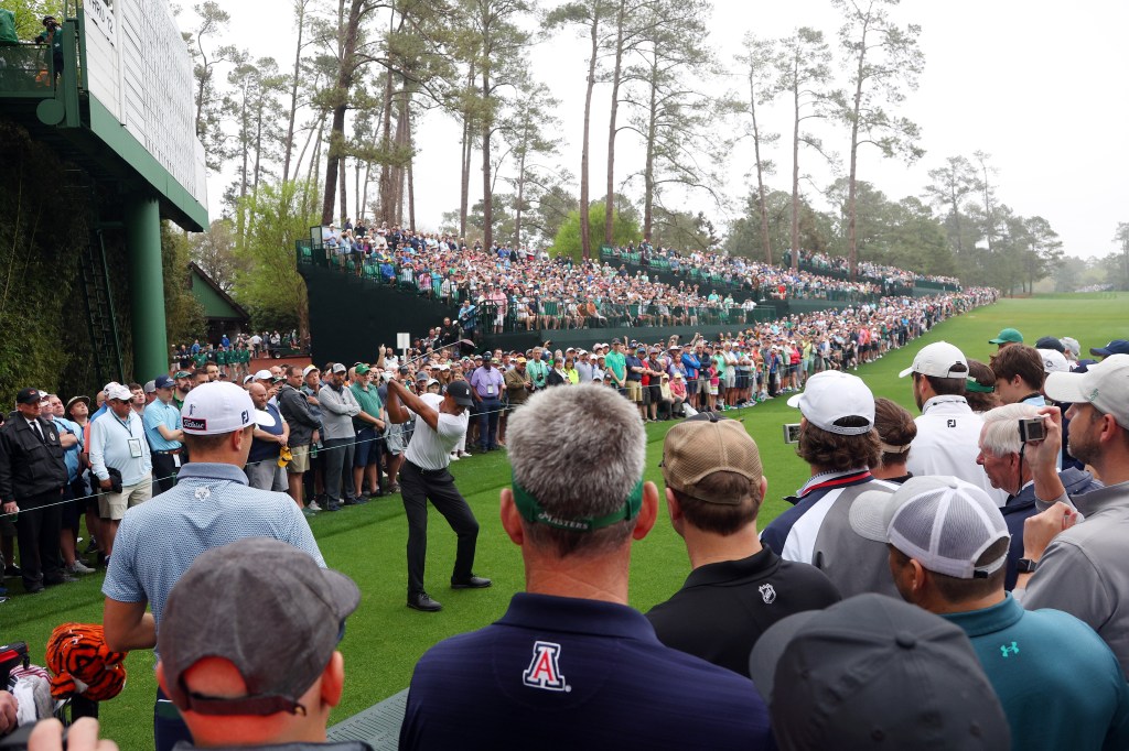 Tiger Woods swinging a golf club on the 14th tee during a practice round at Augusta National Golf Club, surrounded by spectators.