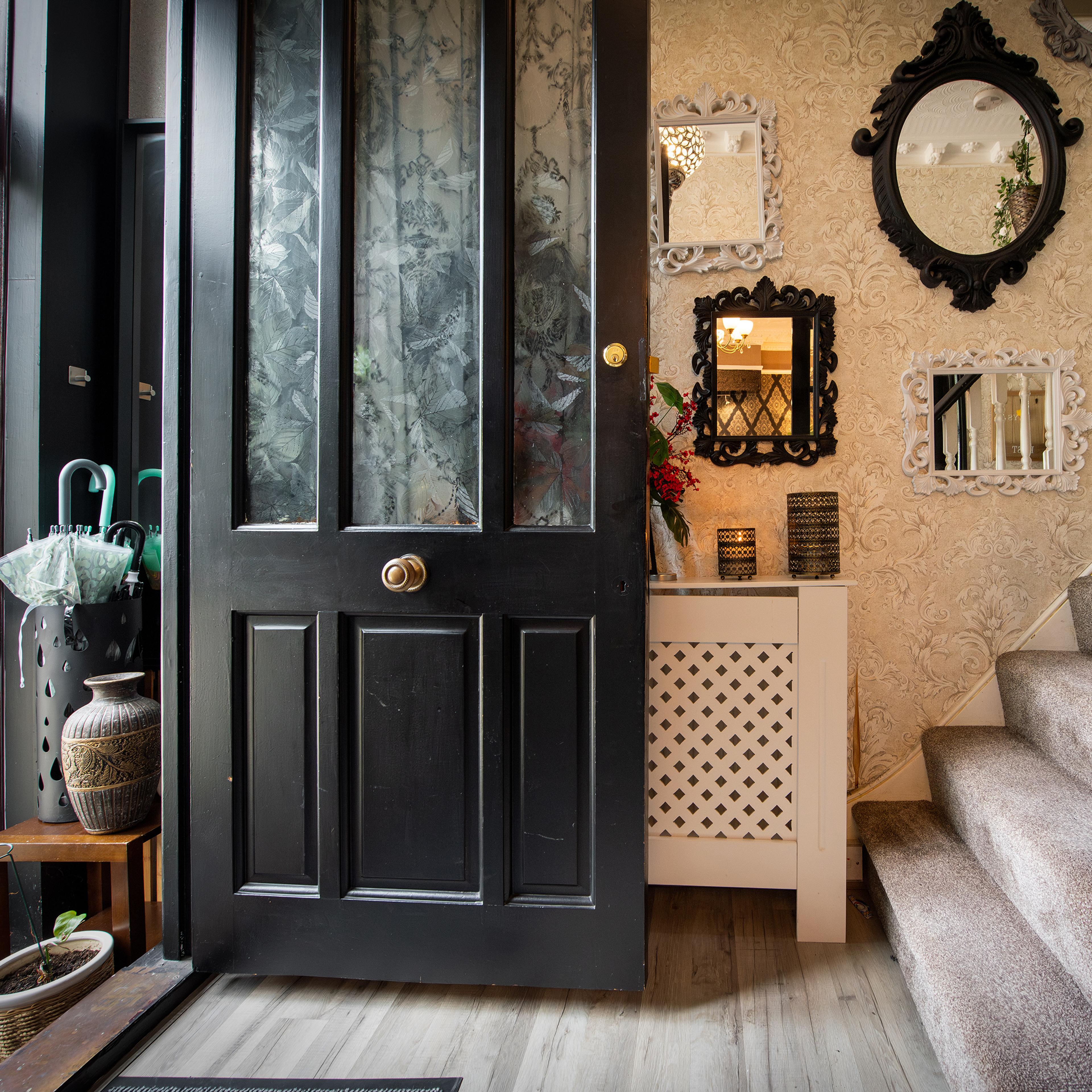 A home entrance with a black front door, mirrored wall, umbrella stand and carpeted stairs.
