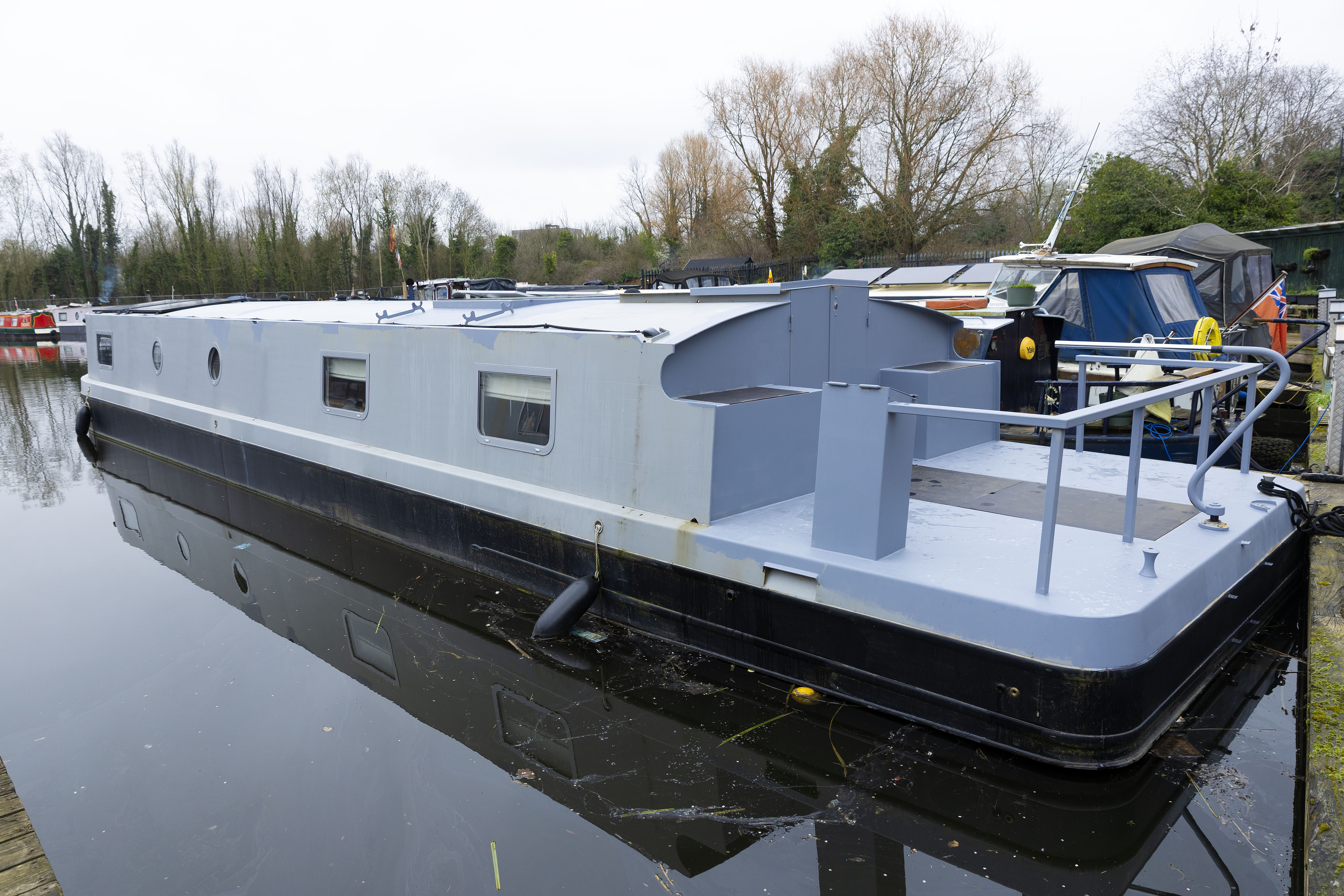 Rosanna Irwin's houseboat, with a light grey upper section and dark hull, docked in west London.
