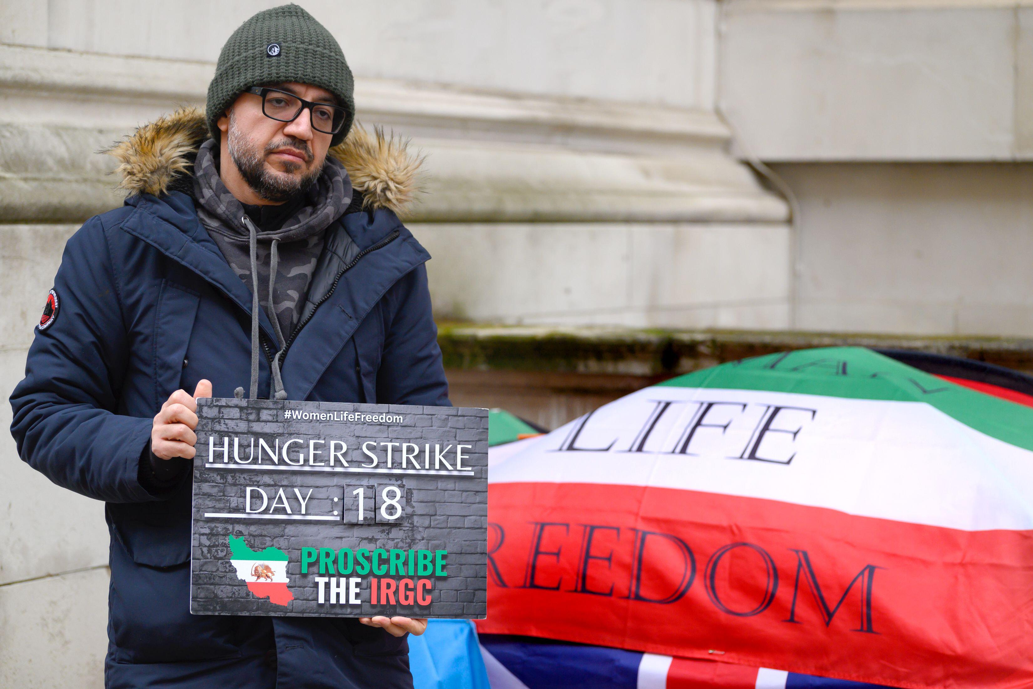 Vahid Beheshti, a journalist and human rights activist, on day 18 of his hunger strike outside the Foreign Office in Westminster, holding a sign that says "Hunger Strike Day 18. Proscribe the IRGC."