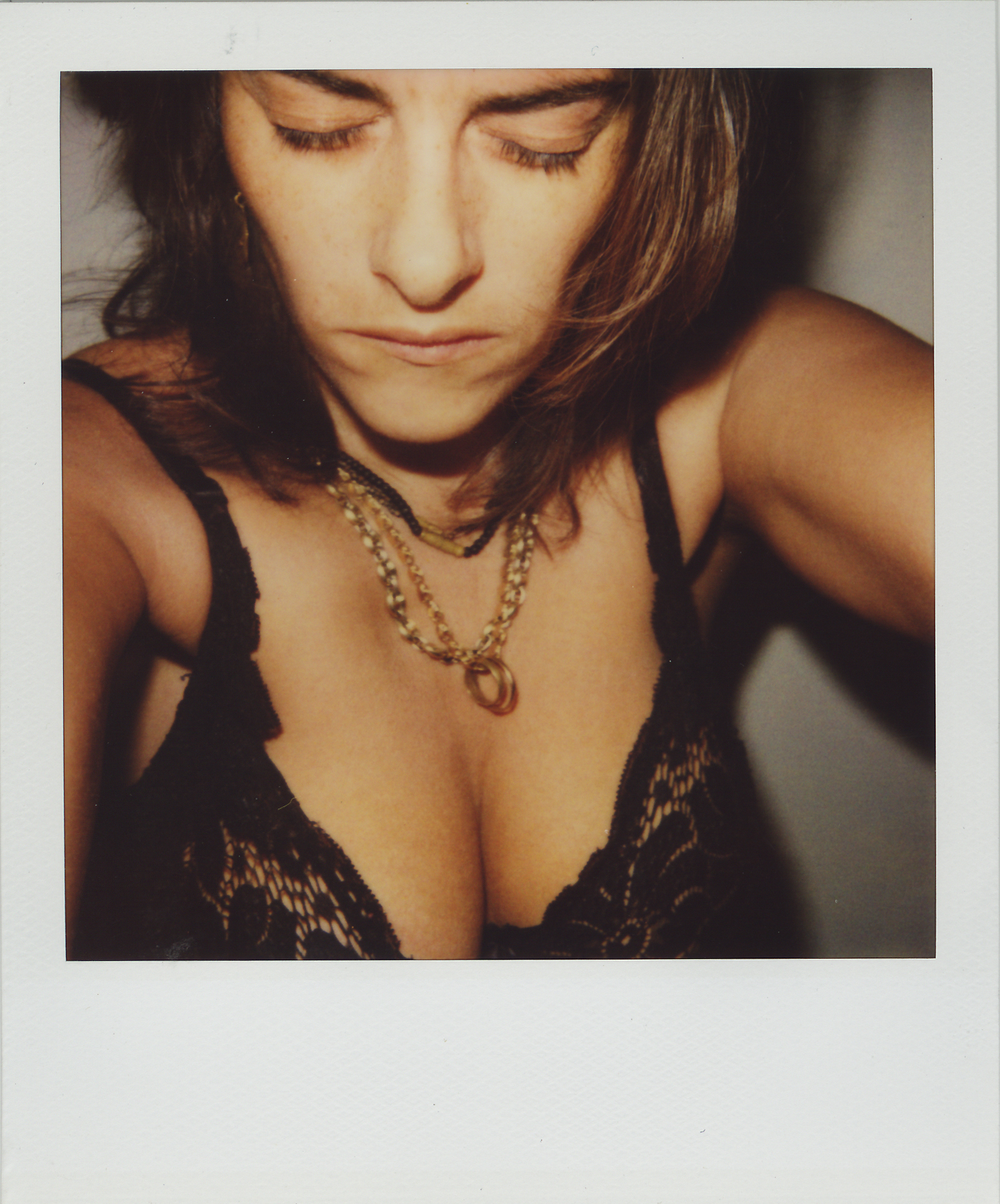 A woman in a black lace bra with eyes closed, wearing a gold necklace.