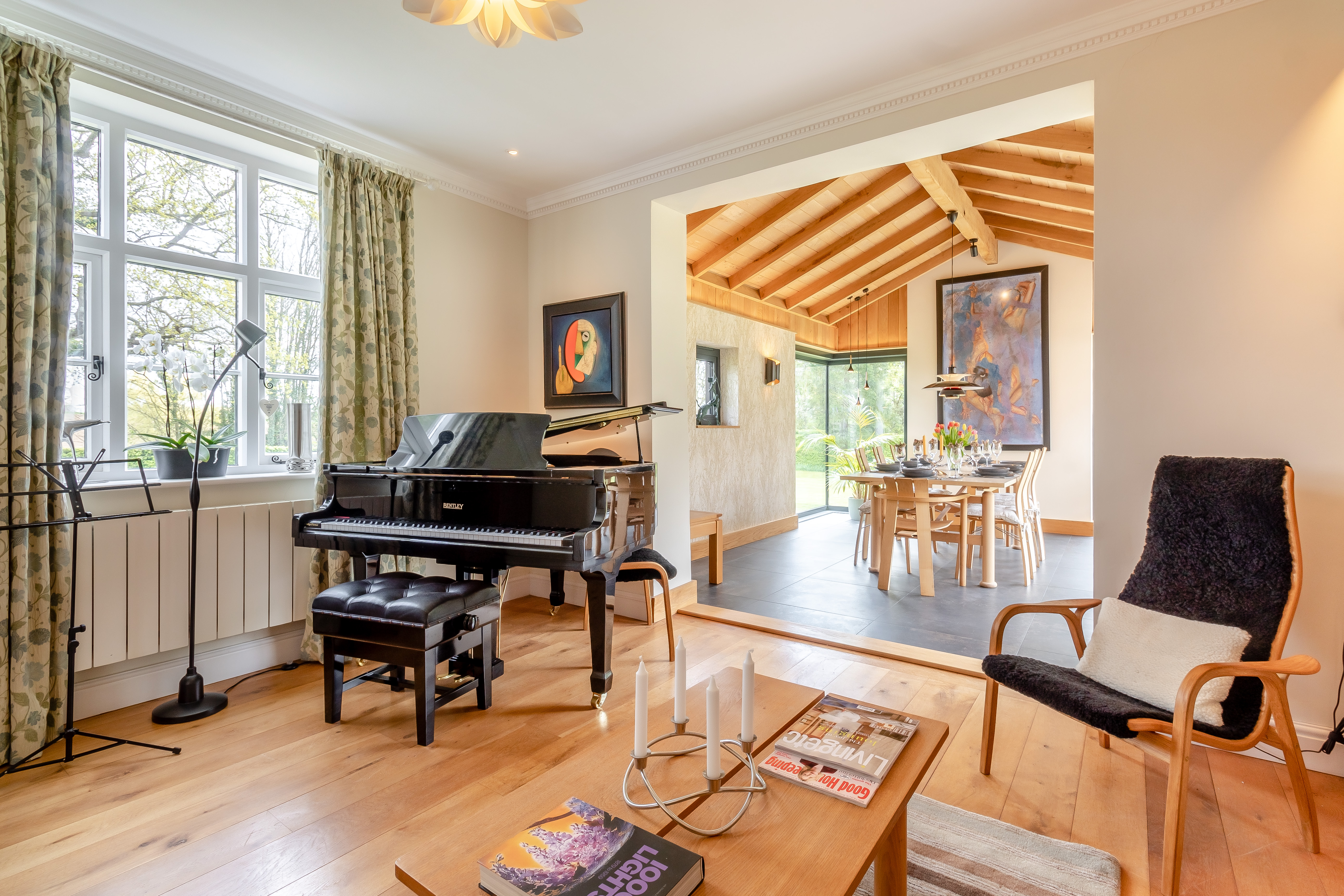 Living room with a black grand piano by the window and a dining room with a large wooden table beyond an archway.