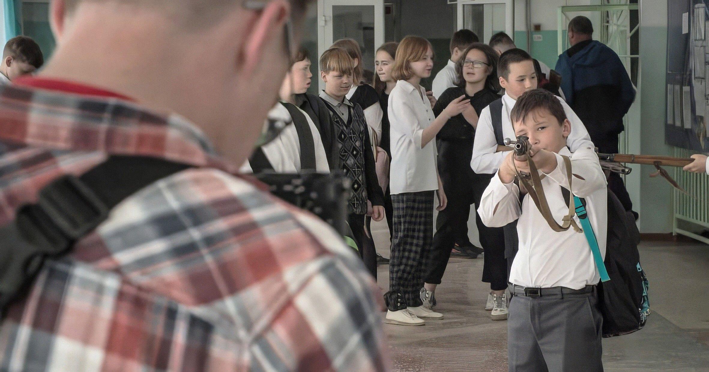 Pavel Talankin with his back to the camera, with a boy aiming a rifle in the foreground, in a scene from "MR. NOBODY AGAINST PUTIN."
