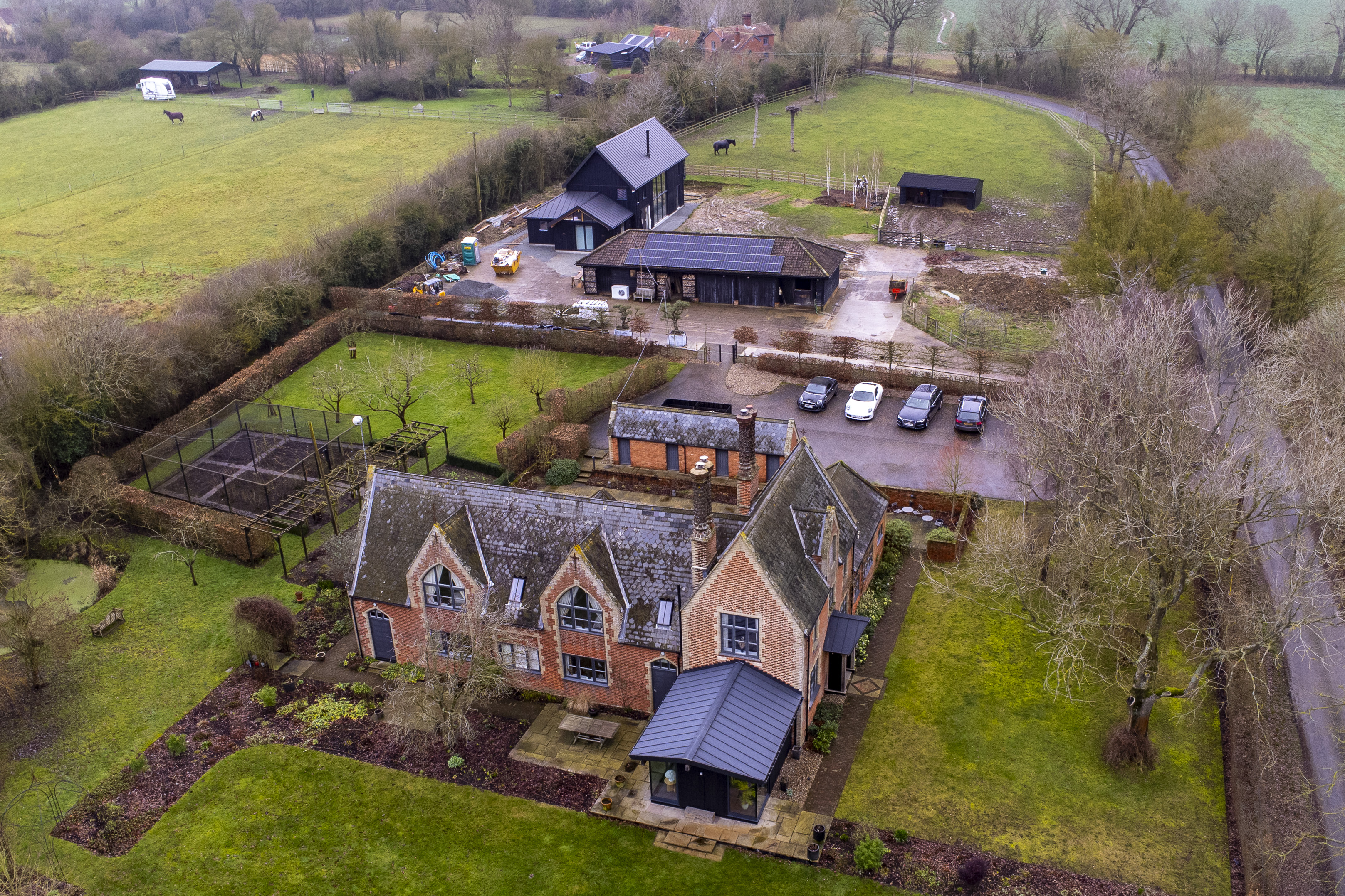 Aerial view of Becks End Farm in Halesworth, UK, showing a large brick house, several modern black barn-like structures, and surrounding green fields.